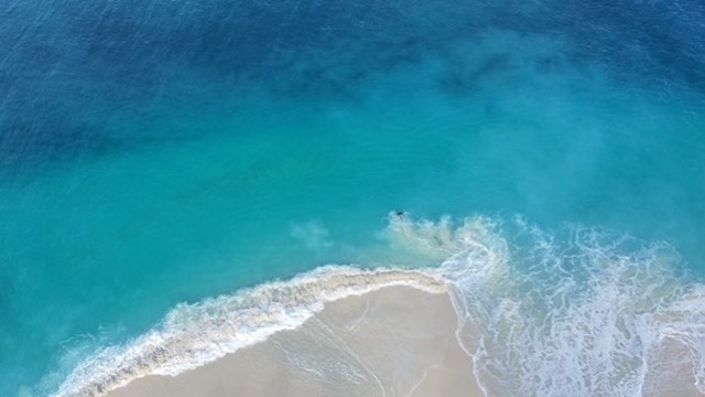 Top-down aerial of turquoise waves breaking on a sandbar